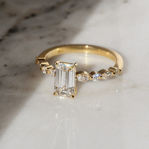 A emerald cut diamond ring placed atop a white surface