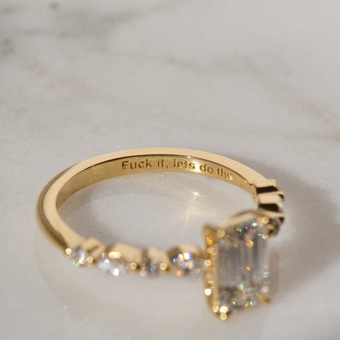A beautiful Gold Ring with Engraving Inside placed on the white shiny reflective surface.