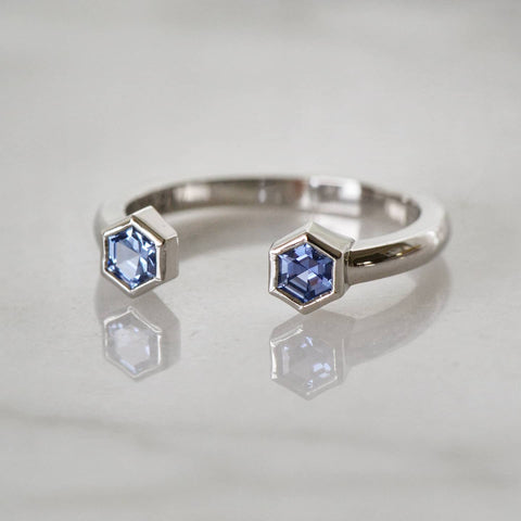 A close-up of a hexagon-shaped blue sapphire open wedding ring placed atop a shiny white surface.