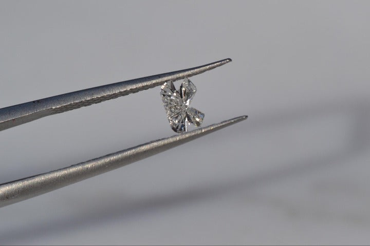 A close-up of a Diamond Initial Pendant held by a tong.