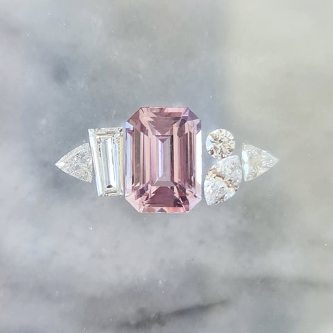 A close-up of a Emerald Cut Pink Sapphire Diamond ring placed on a white surface.