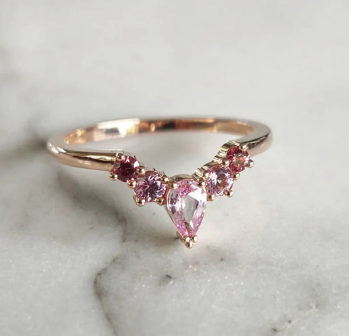 A close-up of a Yellow Gold Pink Sapphire Ring placed on a white shiny white surface.