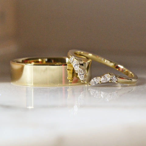 A close-up of a multi stone Yellow Gold Diamond Wedding Ring placed on a white shiny surface.