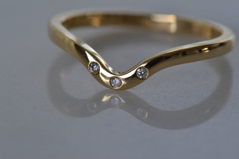 A close-up of a Yellow Gold Diamond Wedding Band placed on the white shiny reflective surface.