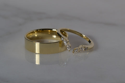 A close-up of a Yellow Gold and Diamond Wedding band placed on the white shiny reflective surface.