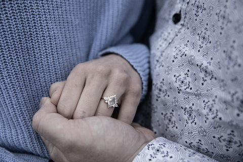 Couple holding hands with focus on a sapphire engagement ring on the women’s hand