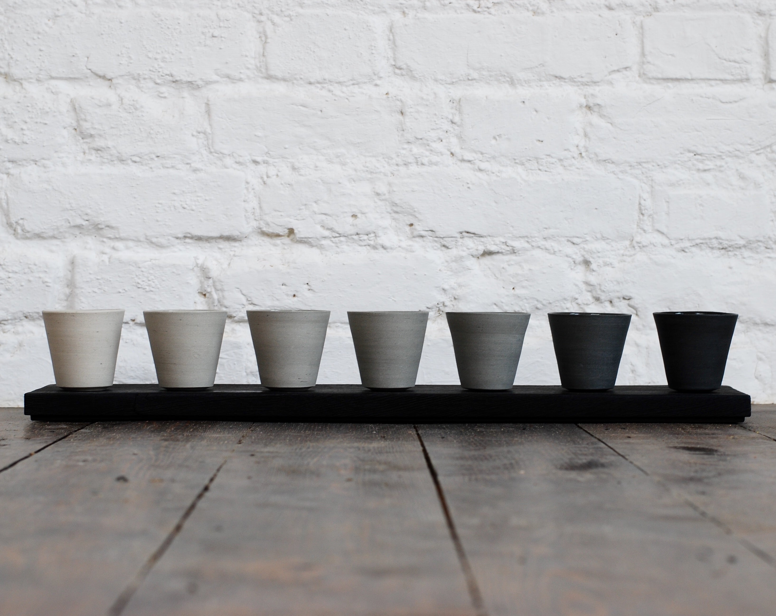 Row of ceramic cups arranged by colour from light to dark by UK-based potter Jono Smart