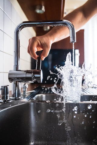 A person pouring water to drink to hydrate their skin