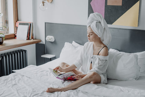 A woman sat on a bed with a towel over her head to dry naturally