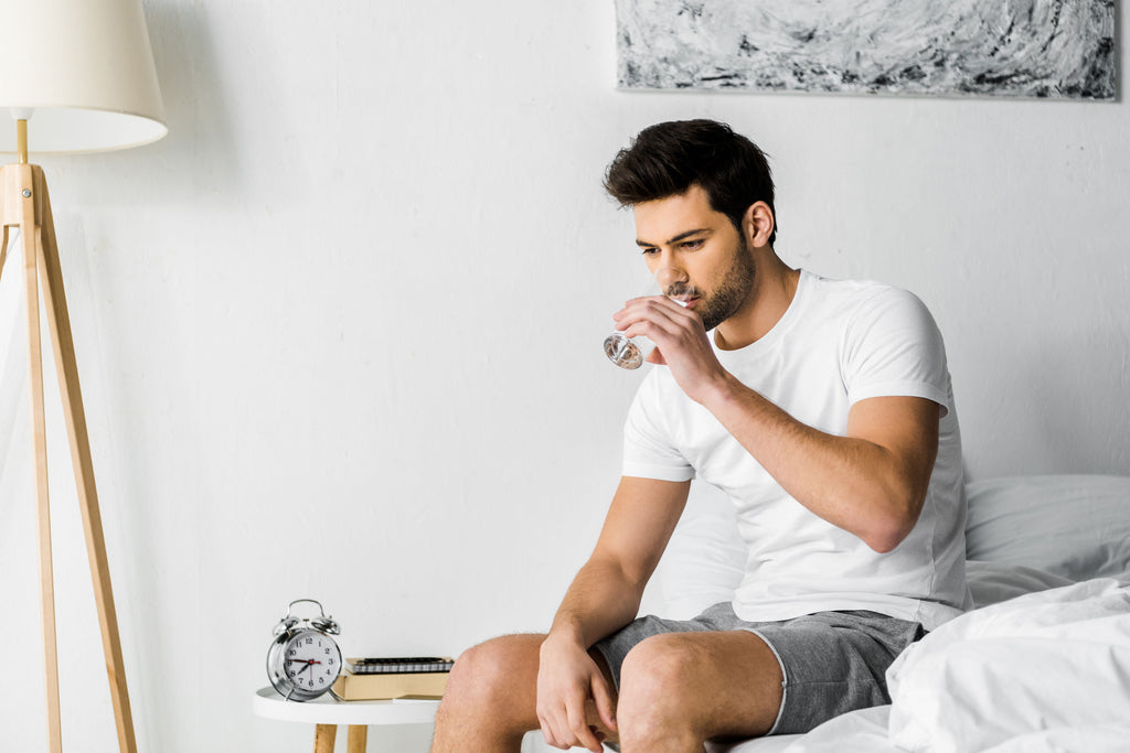Man drinking water while sitting on a bed