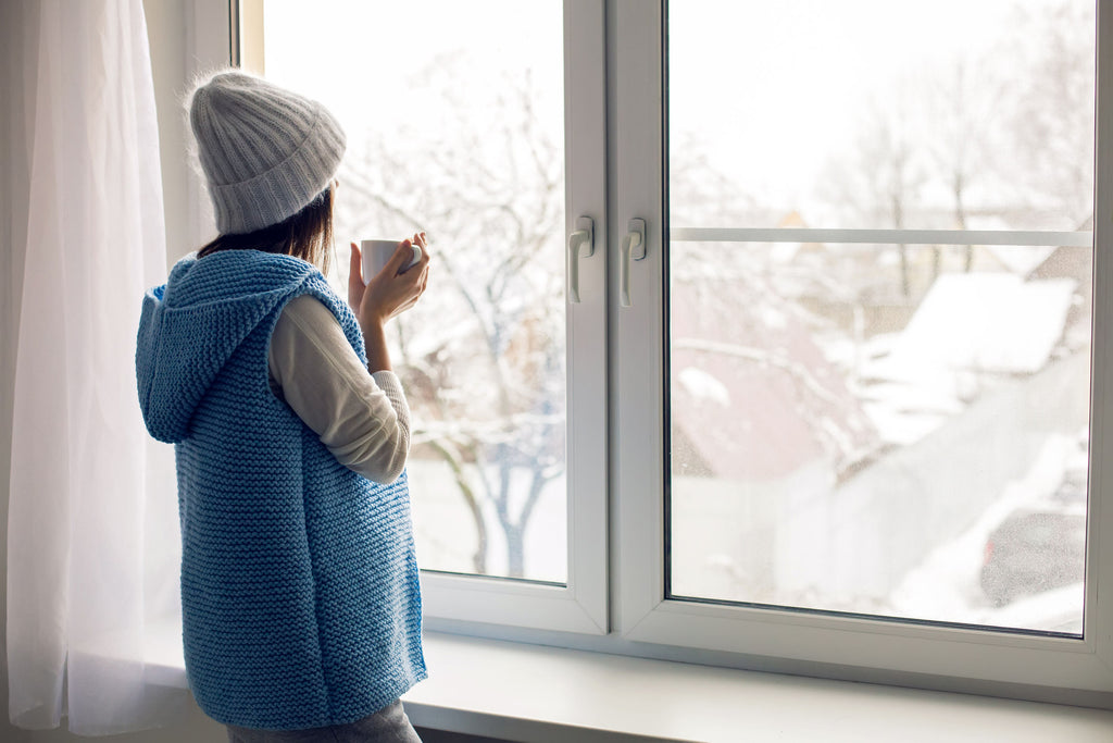 Woman drinking coffee and watching snowfall from window