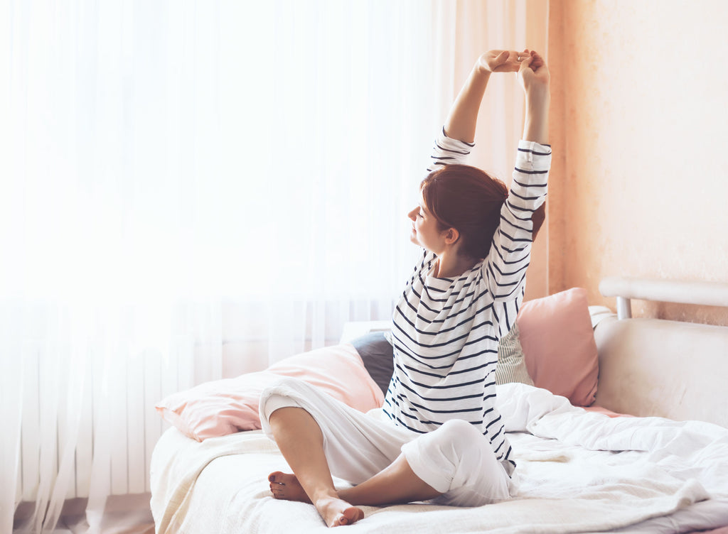 Woman stretching in bed with open smart window blinds