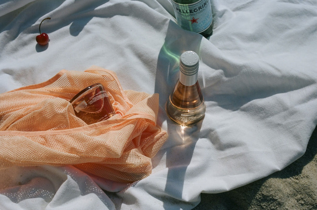 Rose bottle on a white sheet next to a single cherry and Pellegrino