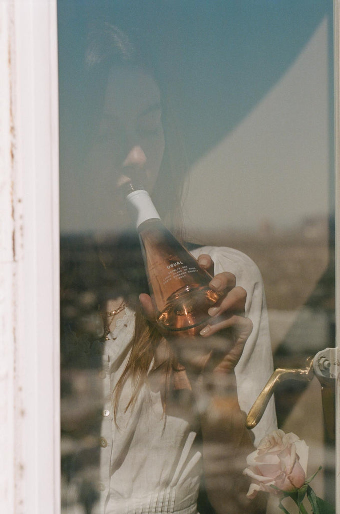 Woman sips on Rose behind a window