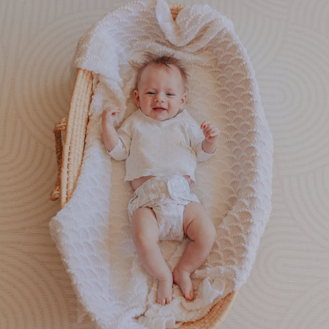 Baby wearing cute modern cloth nappy kicking around in a moses basket