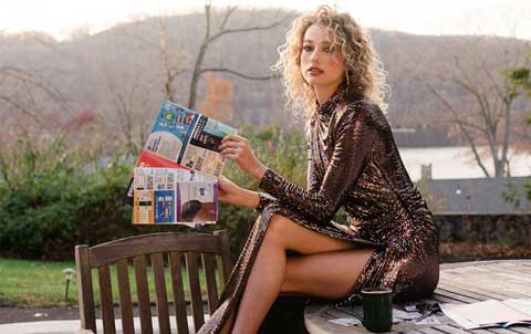 Woman reading a magazine outdoors in a shiny dress.