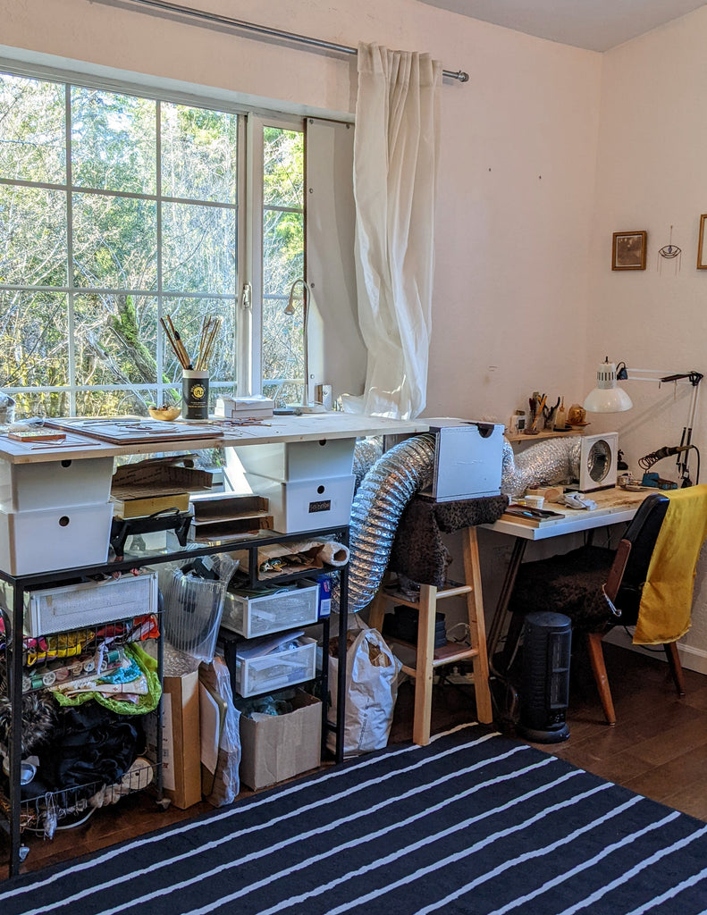 a bright art studio with a striped rug and two tables with supplies on shelves below