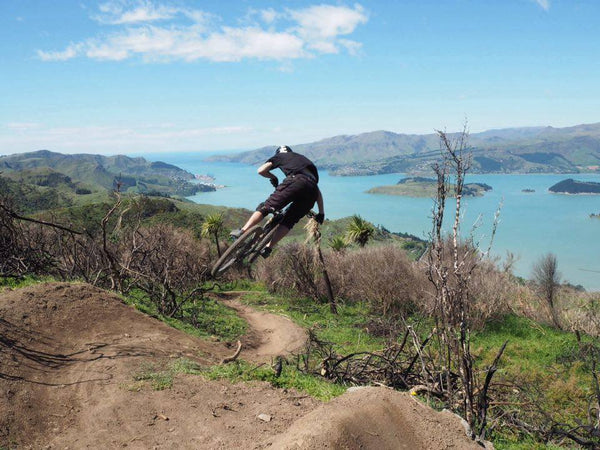 Mountain biker jumping with background of hills and harbor