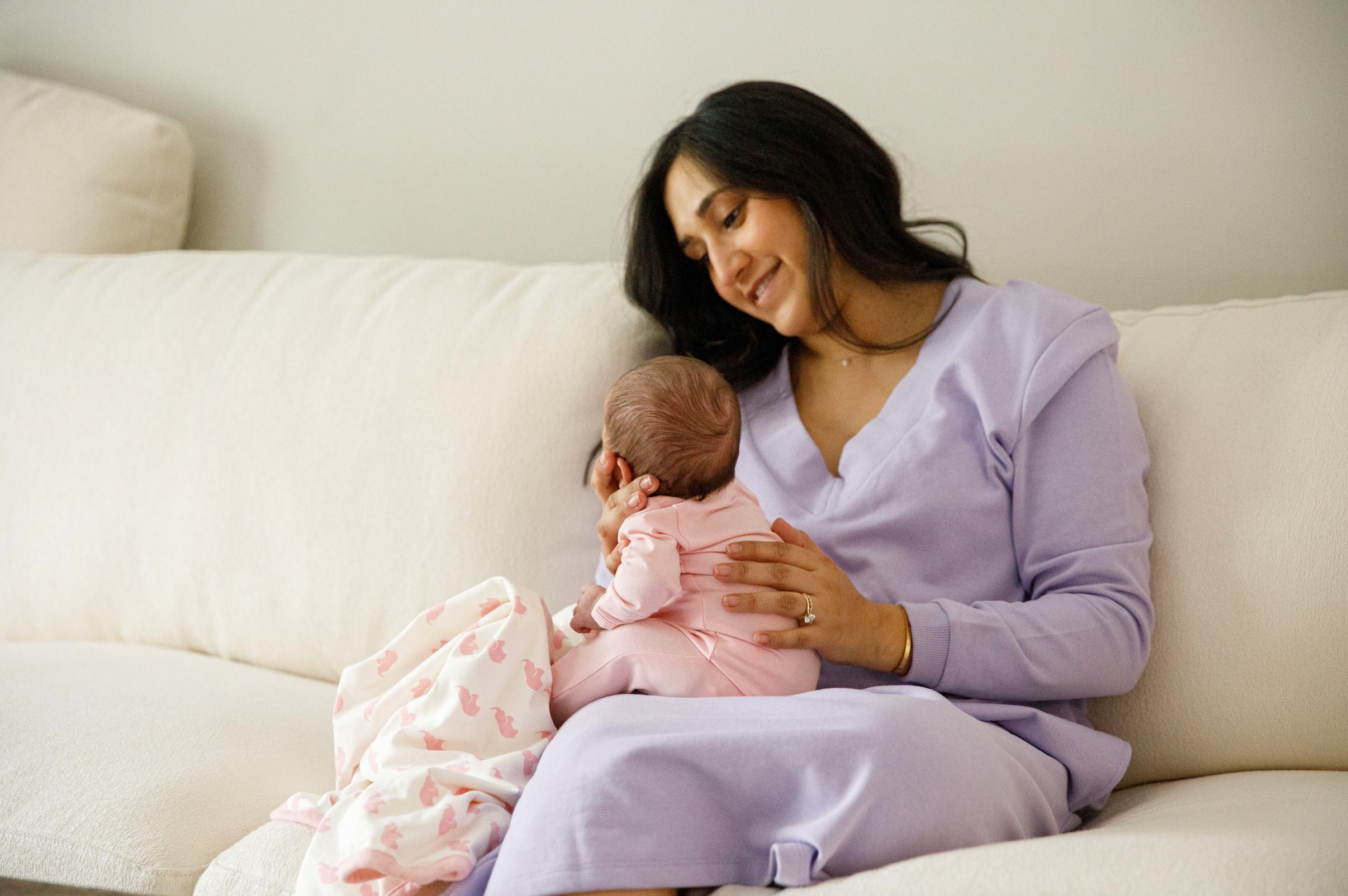 New mom in purple loungewear on couch with baby