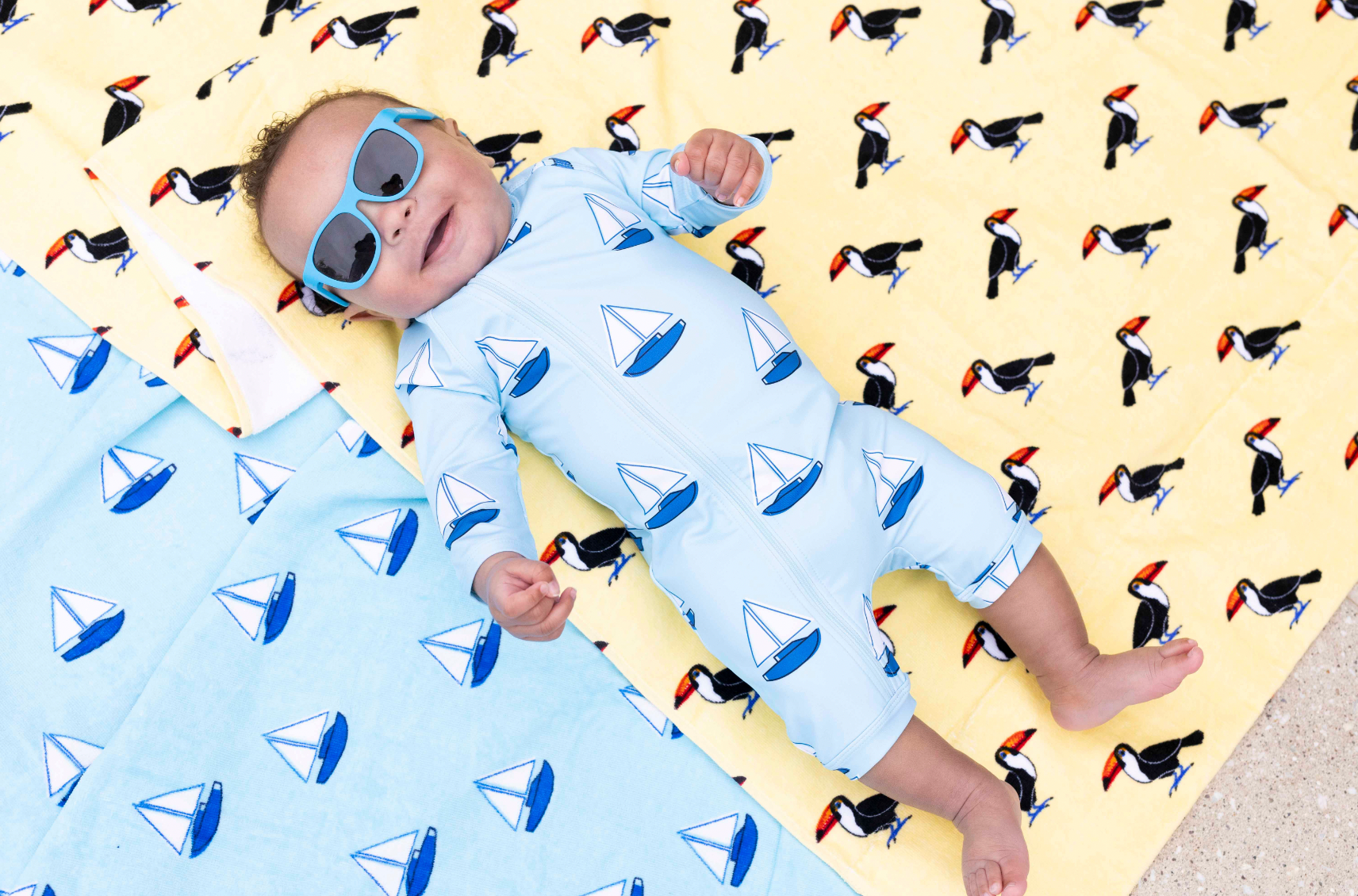 Baby boy wearing sun glasses and laying on towels