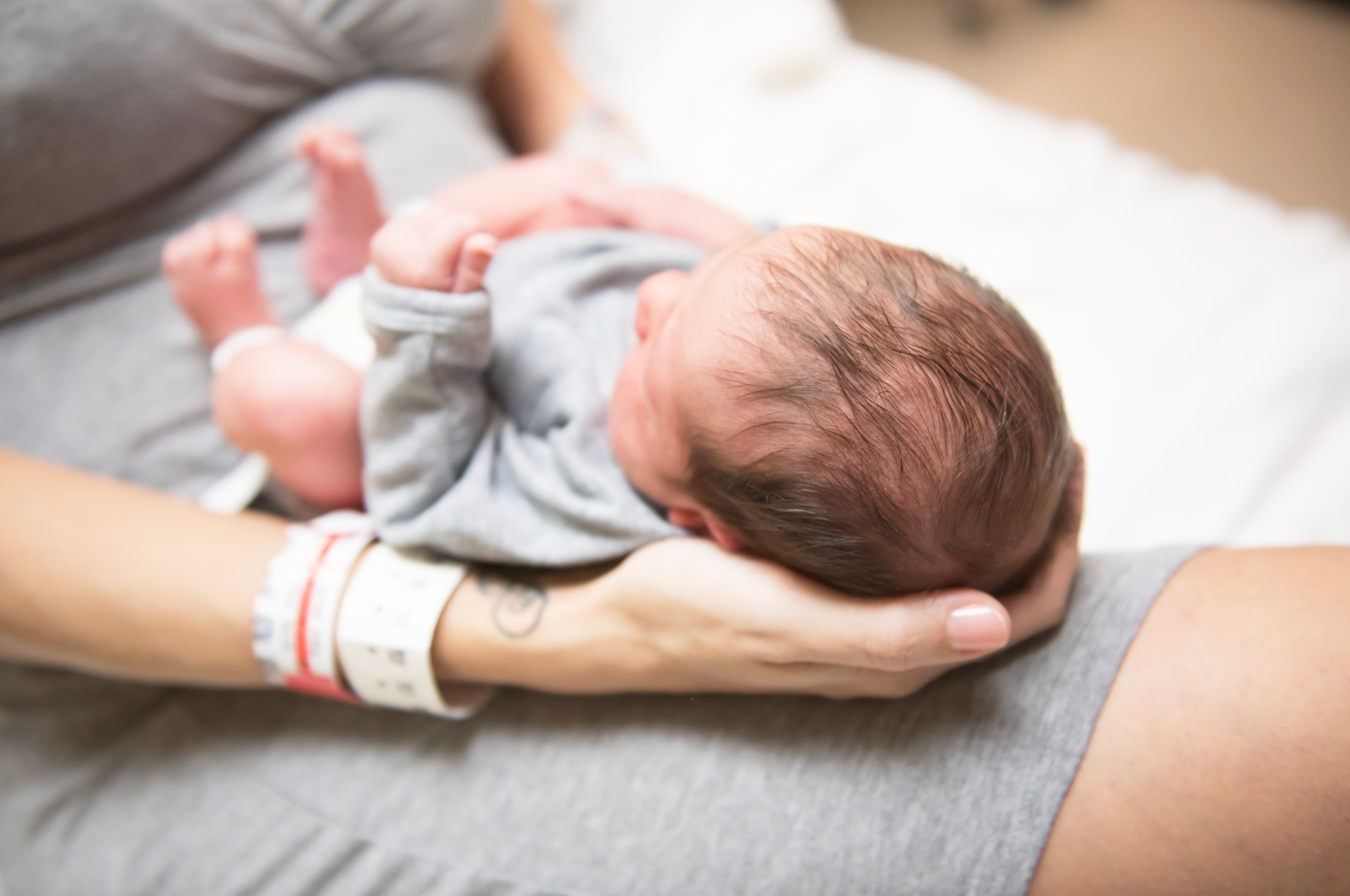 Newborn baby with dark brown hair laying on mom's lap