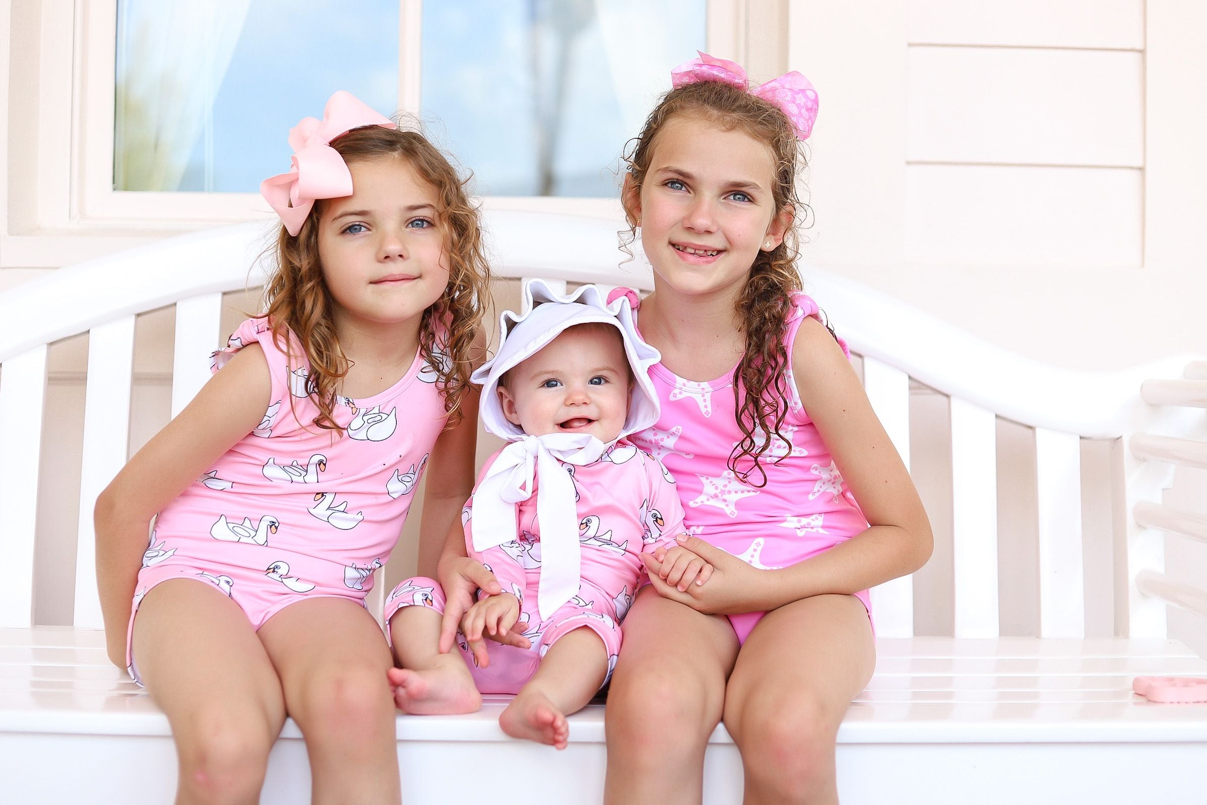 Two girls and baby sister sit outside on a sunny day in matching swimsuits