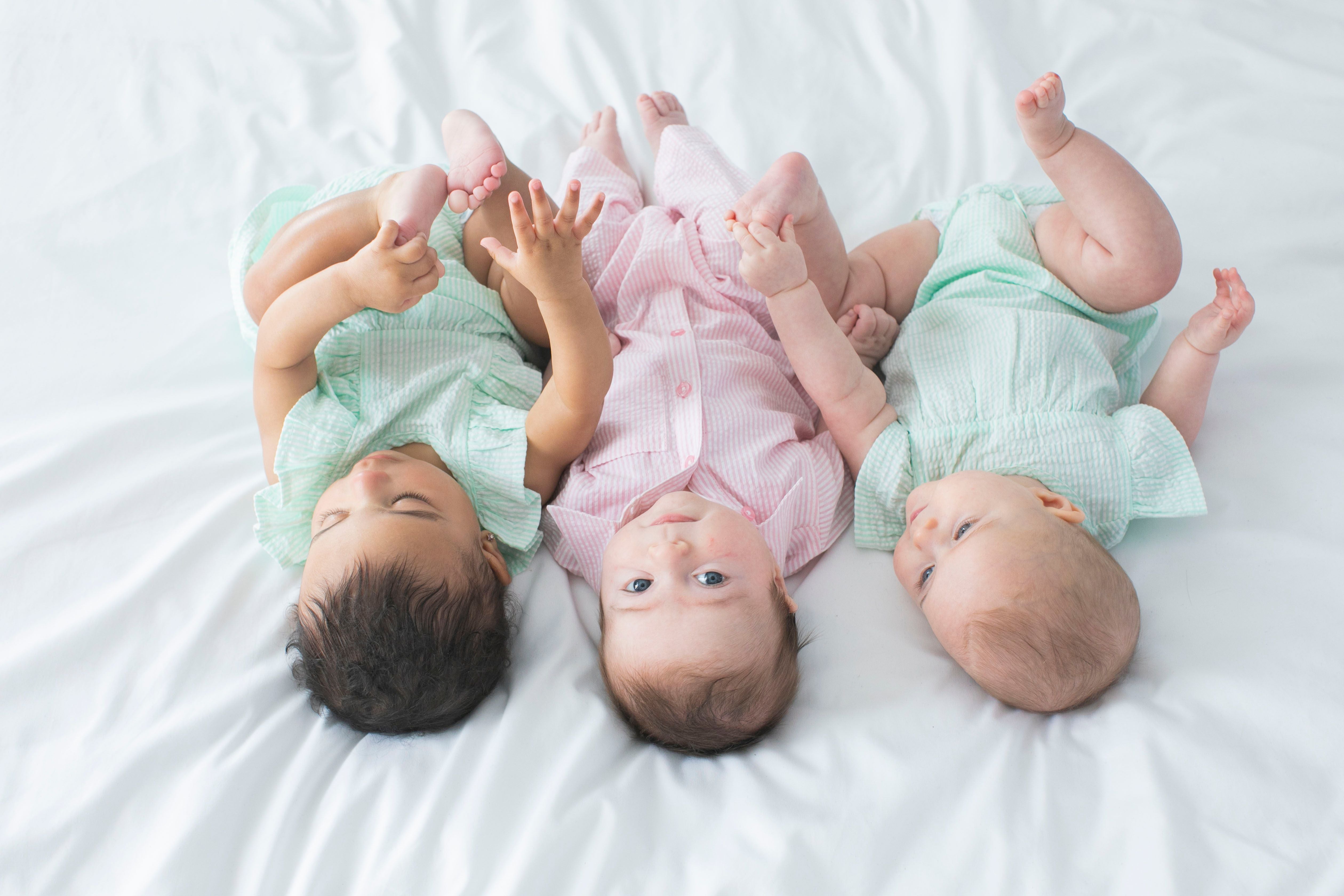 Three babies in multicolored clothing on bed