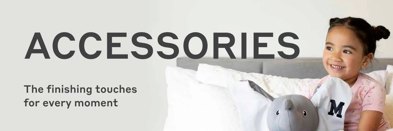 Banner with text 'ACCESSORIES' and subtext 'The finishing touches for every moment', showing a smiling child sitting on a bed holding a gray elephant plush toy.