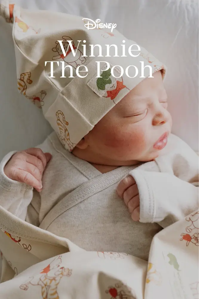 Newborn in Winnie The Pooh print clothing against a neutral background