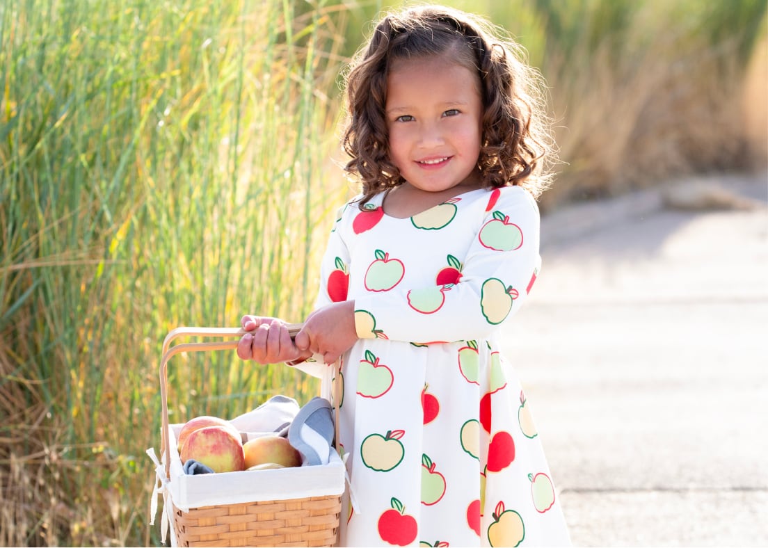 Toddler girl with basket of apples wearing Fall Apples print dress