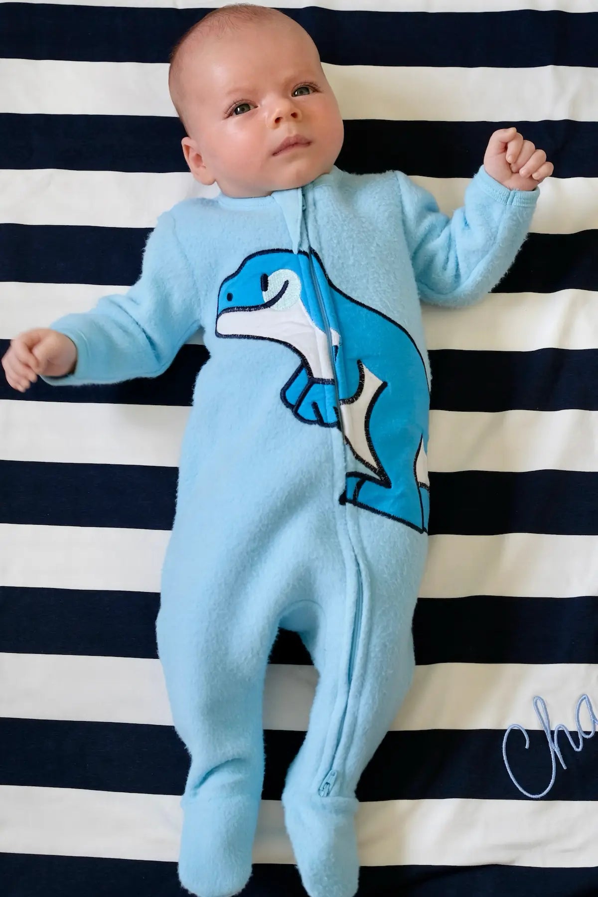 Baby wearing Blue Dino print romper laying on striped blanket