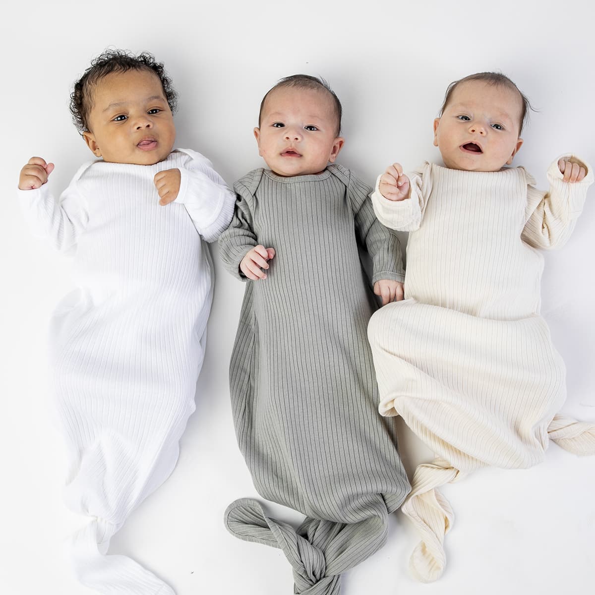 Three babies in sleep bags on neutral background