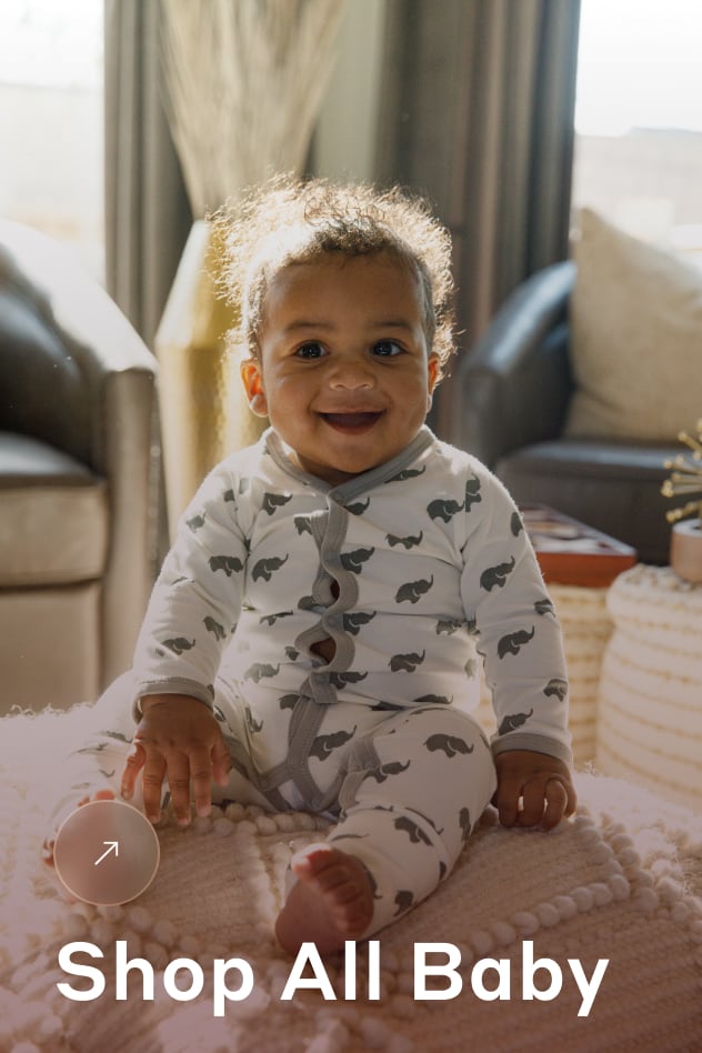 Baby in Grey Elephant romper sitting on bed