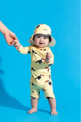 Baby in matching swimwear and hat against blue background