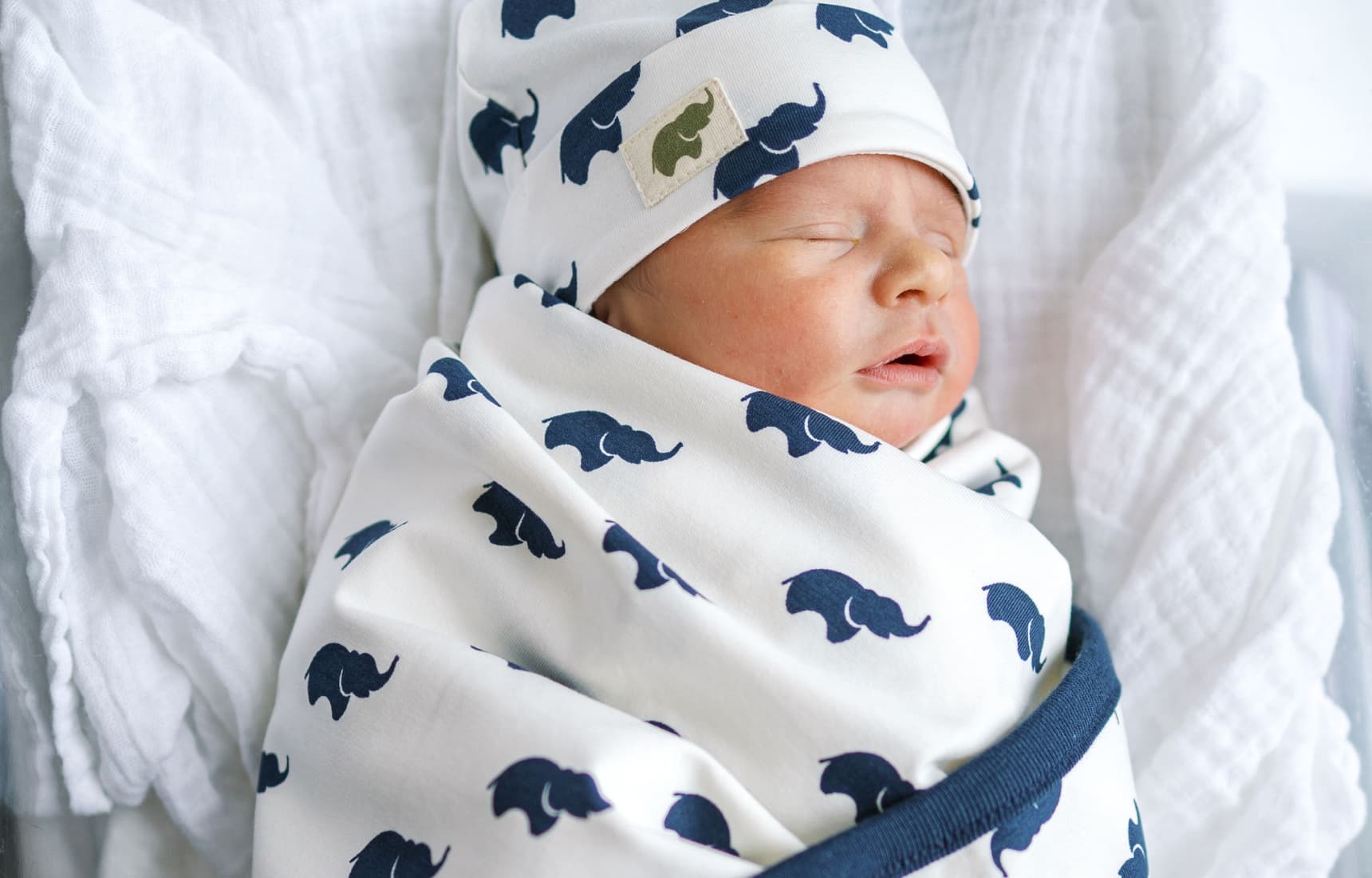 Newborn baby in grey romper stretching on grey stripe blanket