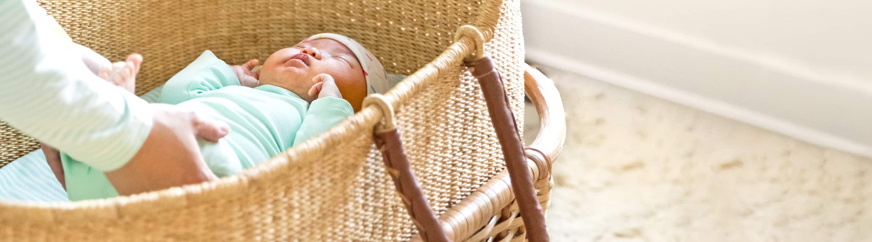 mother reaching for baby in wicker bassinet