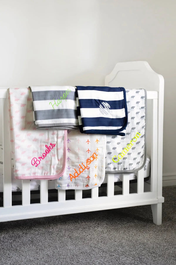 Embroidered blankets hanging on side of crib in nursery