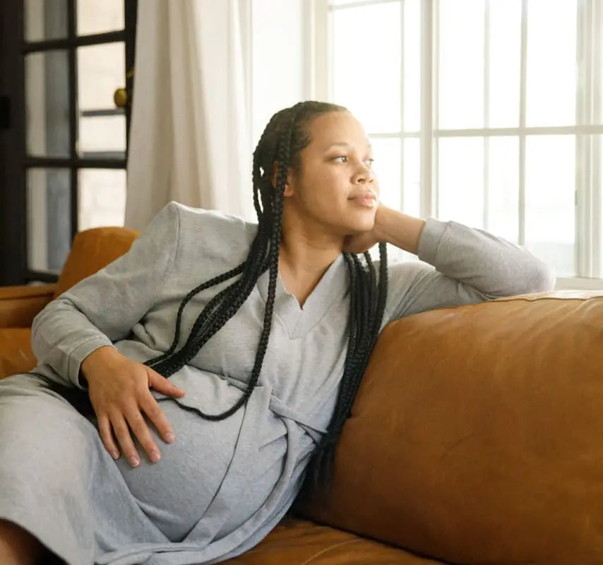 Pregnanty woman holding belly in front of window on couch