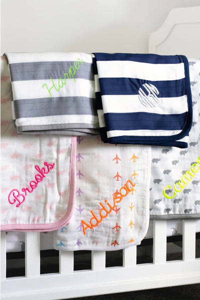 Multiple folded embroidered blankets on crib