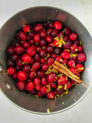 Raw cranberries, cinnamon sticks, and lemon zest in metal pot