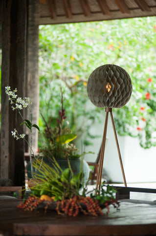 shaded interior shot with bright garden in background featuring bulat standing lamp with shade made of chiffon and linen folds in a sphere atop three tripod teak wood legs.  A little romance mixed with mid century