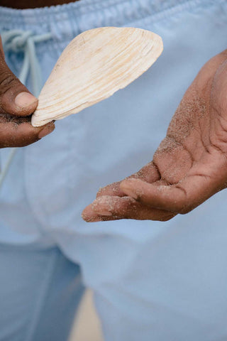 close up of SKU beach short in aqua.  Lucas' hand folding a shell.