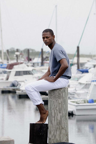 Lucas wearing air force beach terry crew short sleeve sweatshirt and ash corduroy pants.  he is stilling on a pole in a harbor with backdrop of boats parked behind him