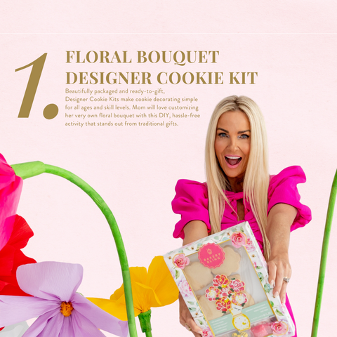 Lauren Brooks, owner and CEO of Bakery Bling, surrounded by large, art-deco flower decorations in a photoshoot setting wearing a vibrant pink dress with ruffles and bows, holding a floral box of Flower Bouquet Designer Cookie Kit for Mother's Day.