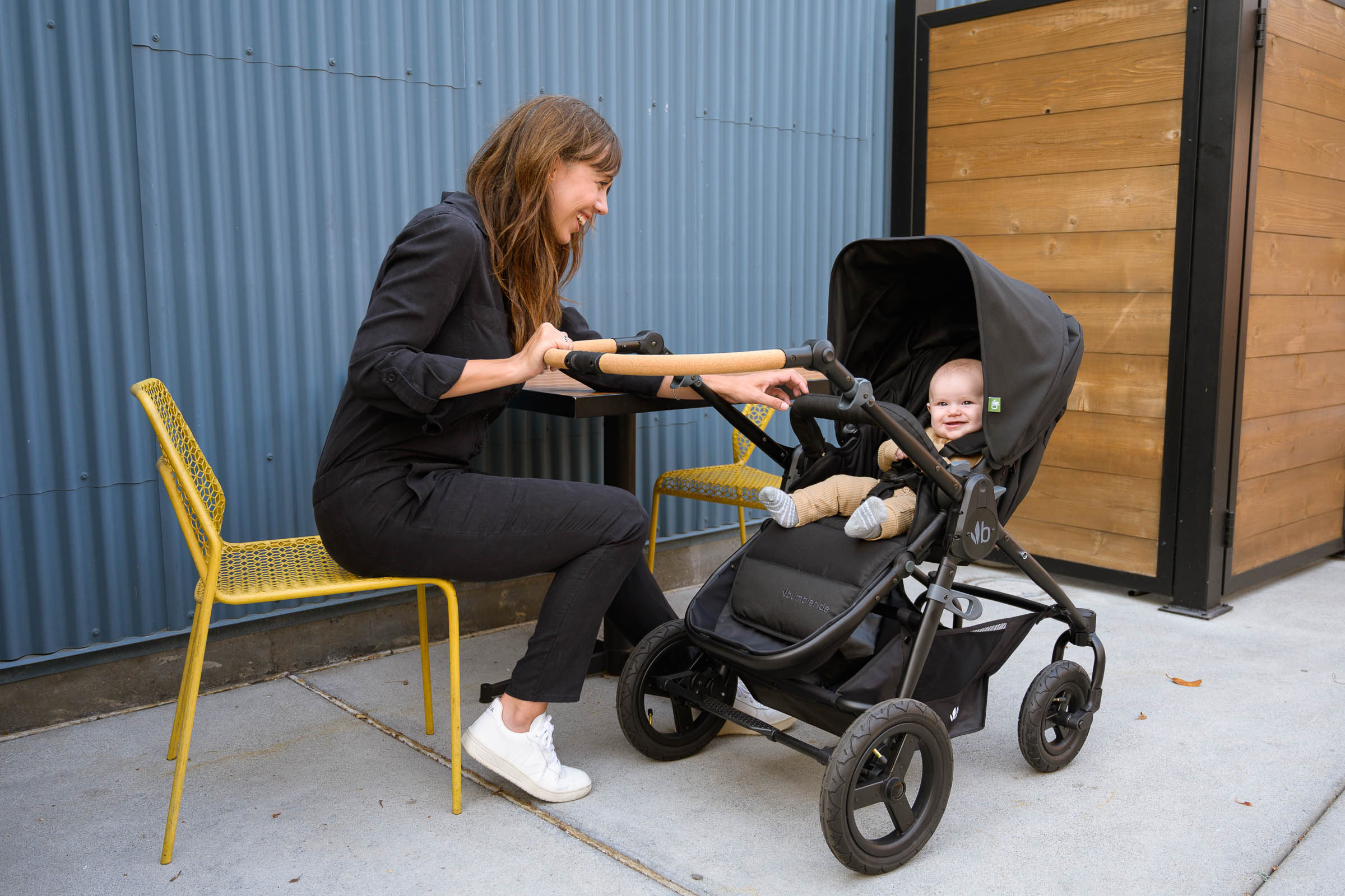 Picture of mother sitting on a chair smiling at her baby sitting in a 2021 Bumbleride Era Baby Stroller in Matte Black