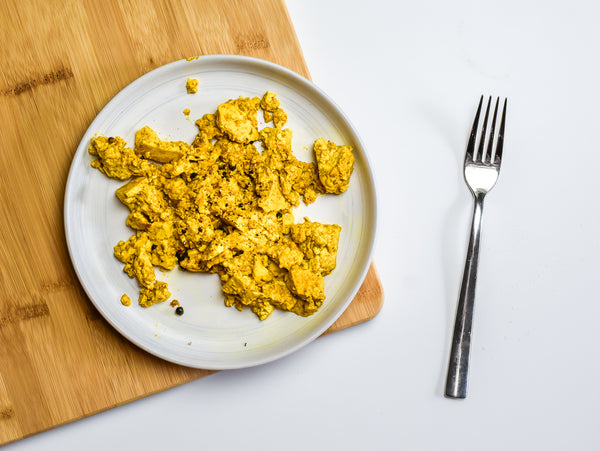 a plate of yellow turmeric tofu sits on a cutting board with a fork next to it