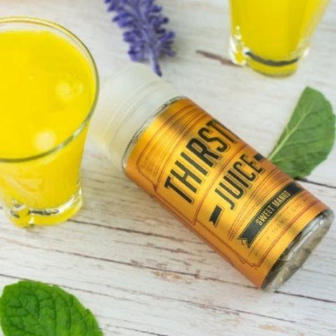Thirsty Juice Co | Sweet Mango 100ml bottle laying on the table with 2 glasses of mango juice and some mint leaves