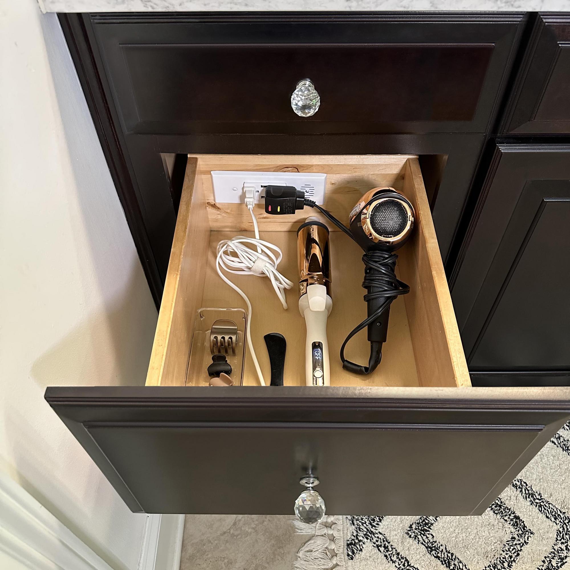 A hair dryer and a curling iron neatly stored in a bathroom vanity drawer, powered by a Docking Drawer Blade in-drawer outlet.