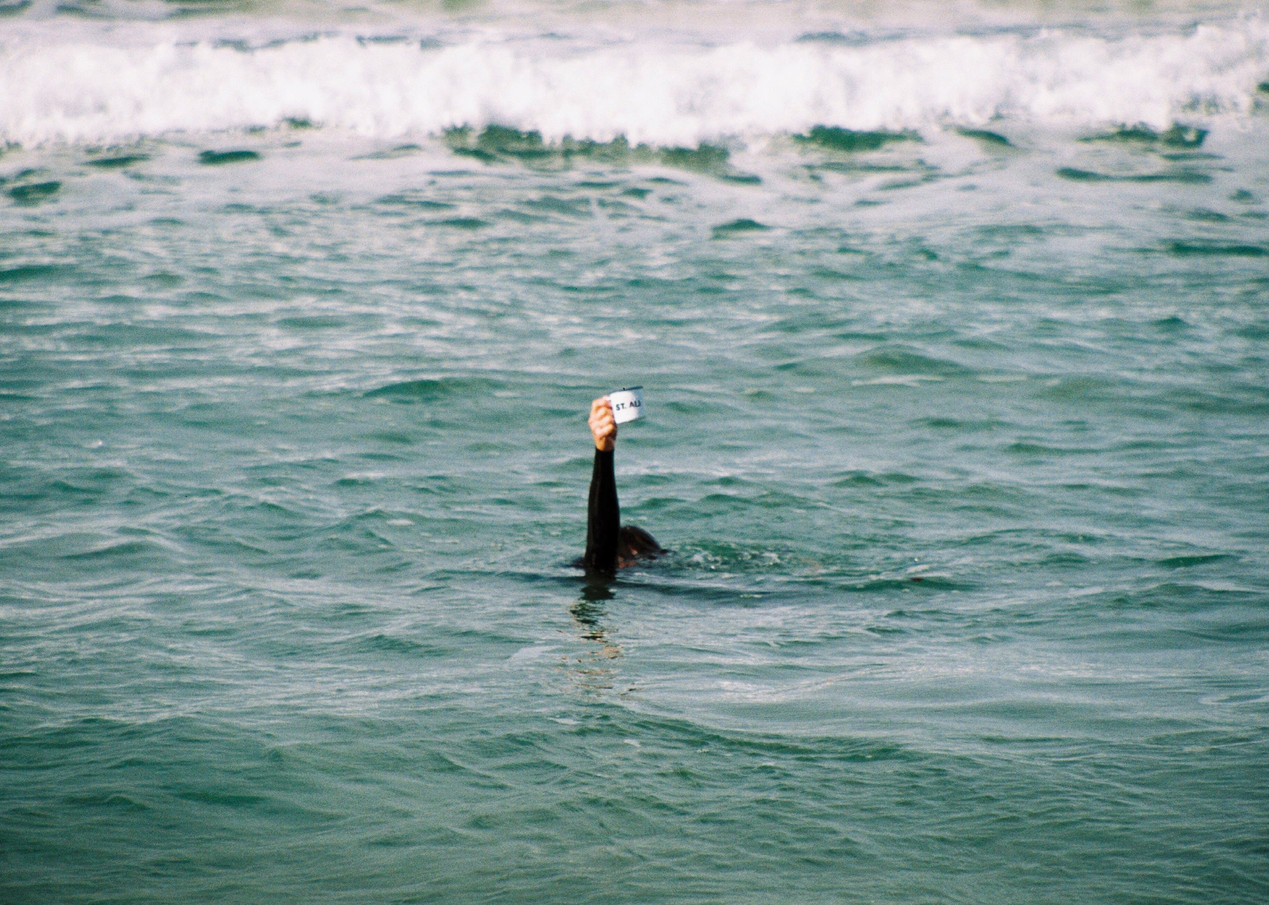 Submerged person holding coffee mug out of water at a beach