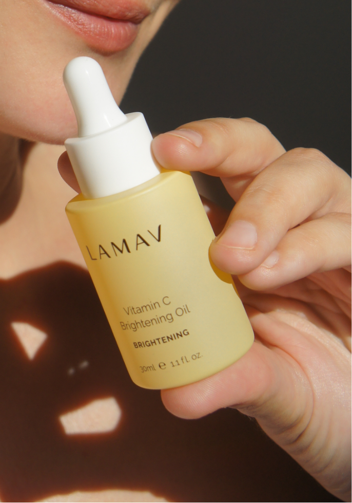 A woman holds a bottle of LAMAV Vitamin C brightening oil, promoting radiant skin with its nourishing properties.